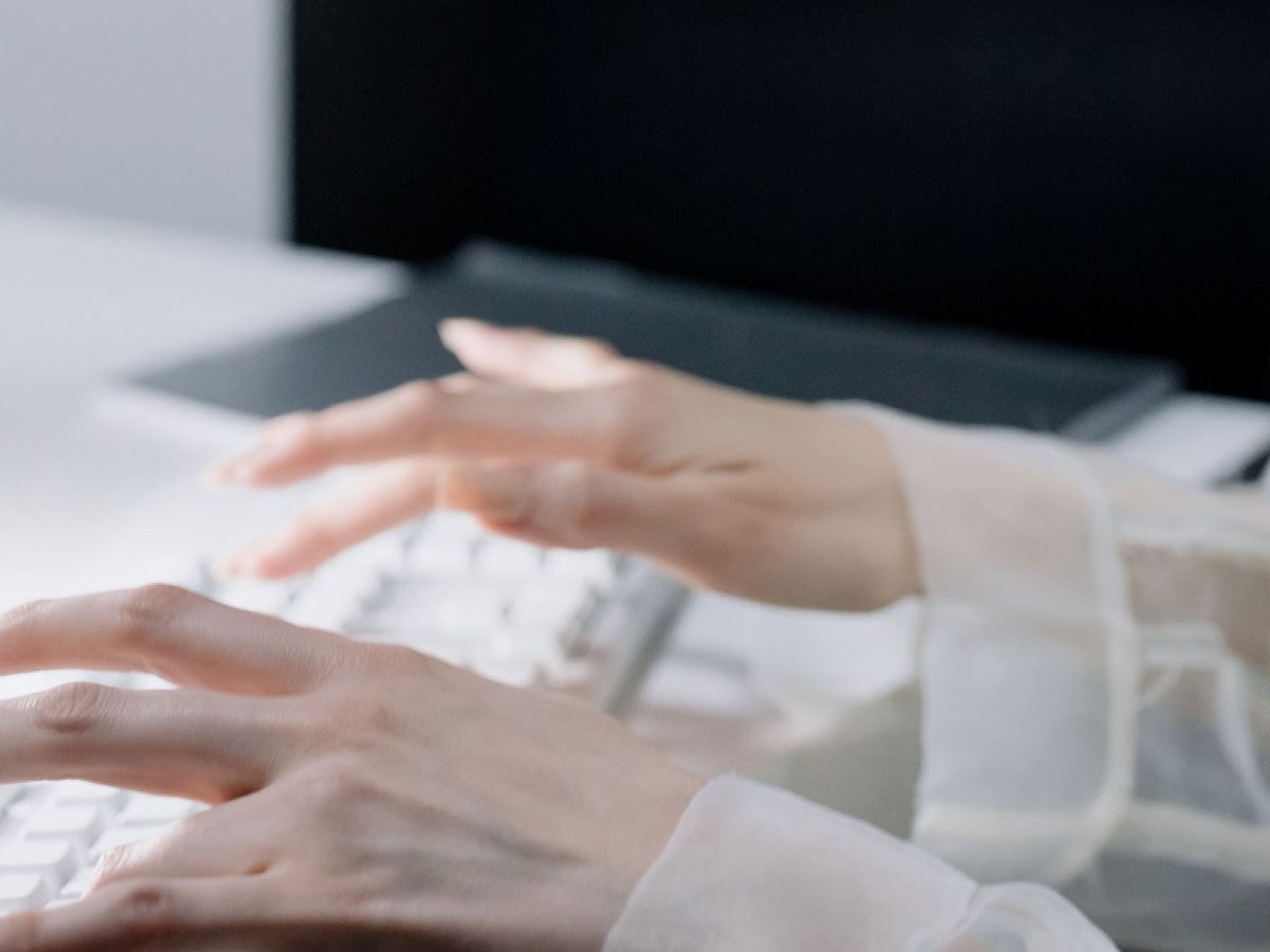Close-up of hands typing at a keyboard, screen in the background.